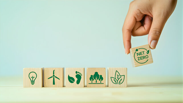 Hand places 'NET ZERO' block alongside sustainable icons, emphasizing commitment to environmental responsibility, green energy, and achieving carbon neutrality