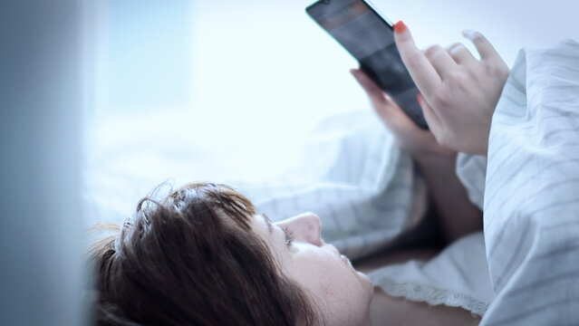 cinematic sleepy brunette woman lies on the bed and uses the phone in the morning, read some informationv