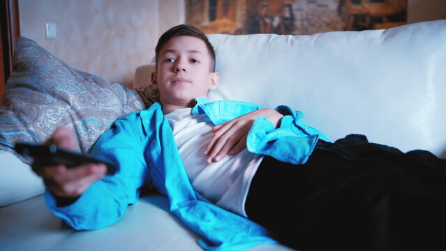 teen boy lies on the sofa watching TV and switching channels, relax on sofa, have fun and enjoy