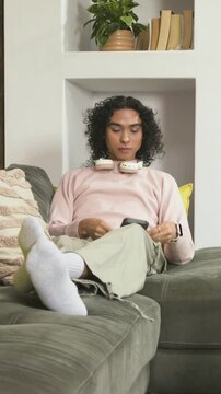 Vertical video: Placing bud on couch person in pink top picking phone donning white headset resting