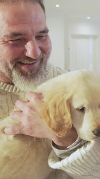Vertical video: Father wearing sweater cradling golden retriever puppy at home, bonding