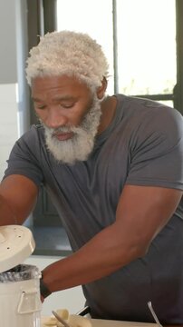 Vertical video: Holding bananas, man in kitchen gray tee loading blender for snack slicing food