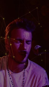 Vertical video: Singing singer in light tee on cue, hitting stick near mic in dim studio with stars