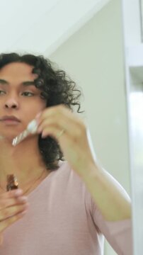 Vertical video: Selecting person in pink top at vanity using amber dropper for skincare under eyes