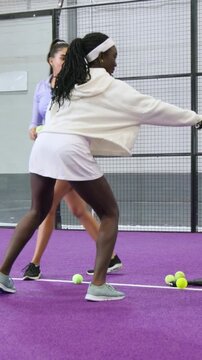 Vertical video: Stepping coach fixing pupil in hoodie on purple court handing racket balls for grip