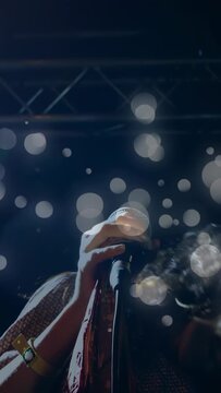 Vertical video: Female singer gripping mic and singing on music stage, bokeh lights overlaying face