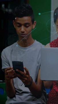 Vertical video: Male teen tapping phone, causing HUD, peer leaning in, comparing screens for class