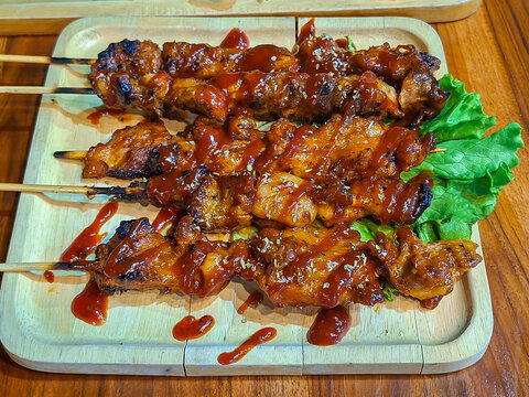 Several skewers of grilled barbecue arranged on a wooden cutting board look very appealing.