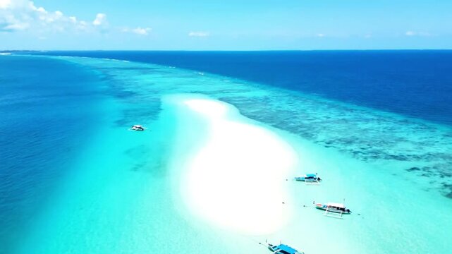 Aerial footage of boats on a pristine white sandbar surrounded by vibrant turquoise ocean waters and coral reefs under a clear blue sky.