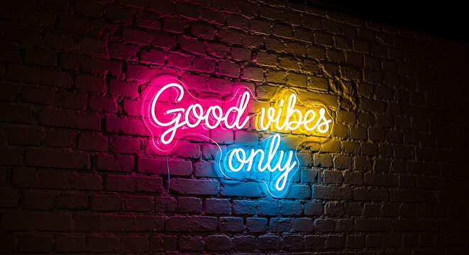 Glowing pink and blue neon sign featuring the text Good Vibes Only mounted on a dark textured urban brick wall background with vibrant electric luminosity and retro aesthetic lighting.