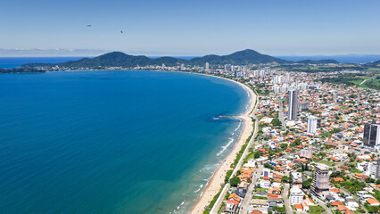 Fototapeta premium Aerial coastal view of Penha with curved shoreline, blue ocean, and dense urban area in Brazil.