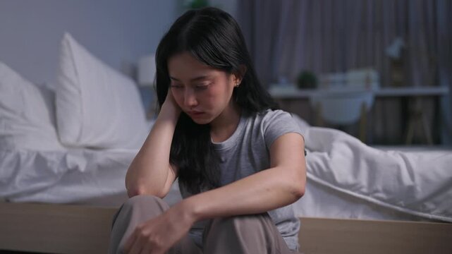 Depressed Asian young woman sitting alone on bedroom floor at night. 