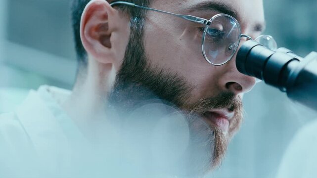 Male scientist examining specimen through microscope lens, concentrating on research in laboratory. Close up view