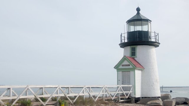 Handheld shot of Brant Point Lighthouse in Nantucket, Massachusetts, with a small motorboat cruising past the calm harbor under soft coastal daylight.
