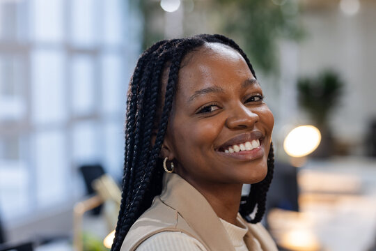 African American woman smiling over shoulder at office with desk lamp, plant, windows, copy space