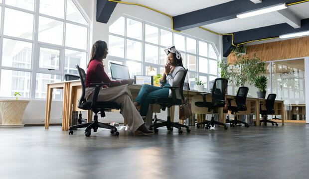 Diverse female coworkers typing on laptops and one wearing head-mounted device in coworking office