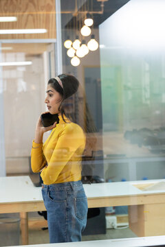 Indian woman holding smartphone to ear and standing beside worktable in modern office