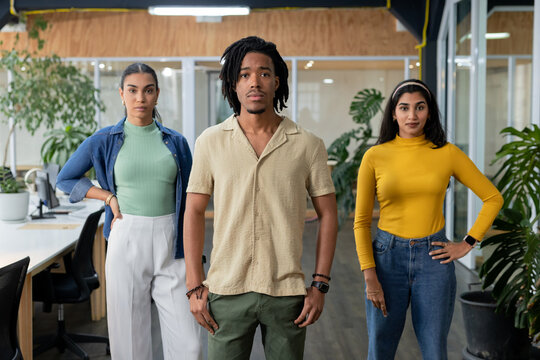 Diverse coworkers standing confidently in modern office with computer monitors and potted plants