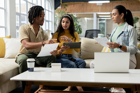 Diverse coworkers collaborating around charts and tablet on sectional sofa in office lounge