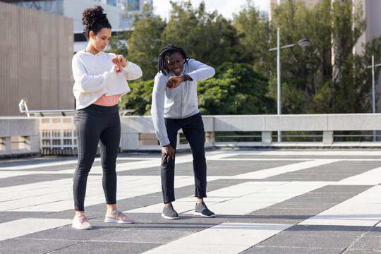 Diverse friends on patterned plaza pavement checking wristwatches near concrete railing