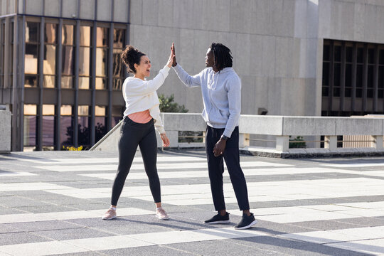 Diverse workout partners high-fiving on rooftop plaza featuring checker tiles, barrier railing