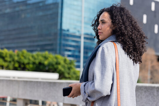 Woman in overcoat checking smartphone on terrace with bag, copy space