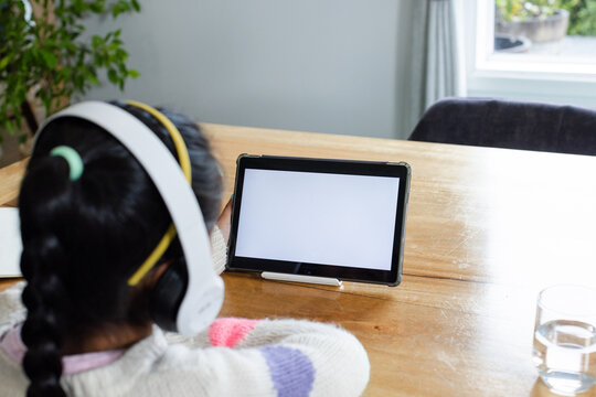 White over-ear headphones are resting on wooden table beside tablet stand and glass of water