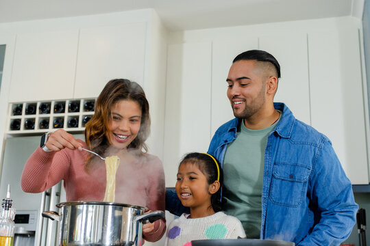 Family stirring steaming spaghetti noodles in bright modern kitchen with steel pot on stove