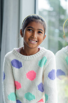 Asian girl smiling, sitting at home by window in white sweater with polka dots, yellow headband