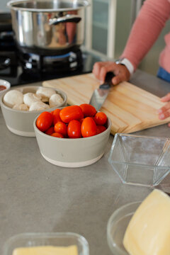 Mid adult woman slicing vegetables on cutting board in home kitchen with chef's knife and bowls
