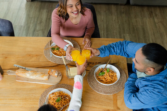 Family raising glasses and sharing meal at home dining area with spaghetti, baguette, placemats