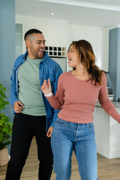Couple dancing playfully in modern kitchen with wine rack, potted plant and island countertop
