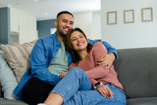 Couple sitting on gray fabric sofa in modern living room near kitchen, showcasing smartwatch