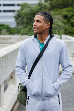 African american man in twenties in hoodie standing on terrace with olive green shoulder bag