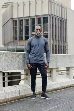 African american man leaning on concrete railing on urban walkway in sportswear and smartwatch