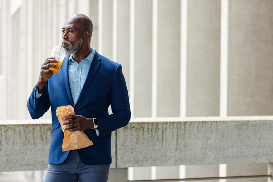 African american man standing in walkway holding paper bag and sipping orange juice