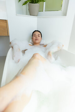 African-American female lying in tub resting on towel foam covering torso plant-at frosted-window