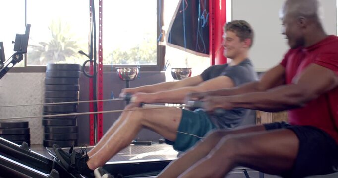 After grabbing handles diverse male partners rowing in gym, sharing smiles