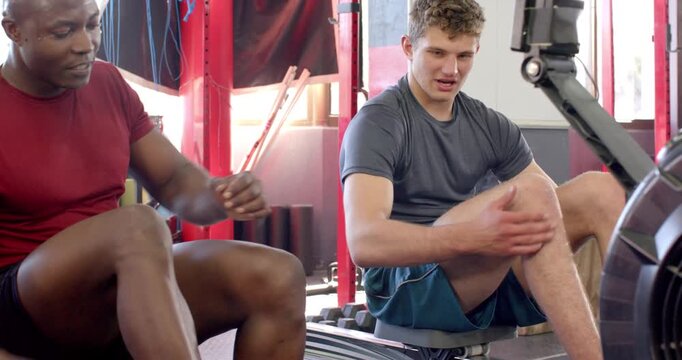 Diverse male friends pulling rowing machine handles in crossfit gym after