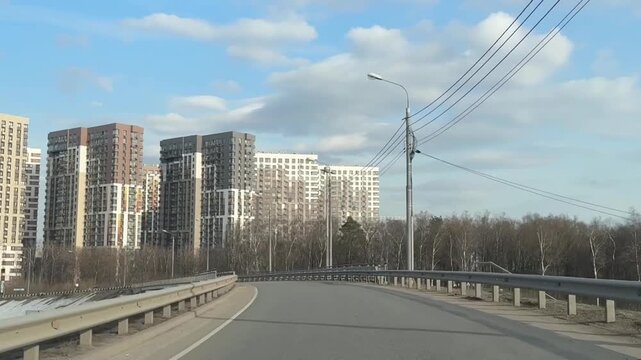 Driving along a curved urban road past modern apartment buildings, streetlights, and roadside trees in clear daytime in Odintsovo, Russia,  from a moving car perspective. High quality FullHD footage