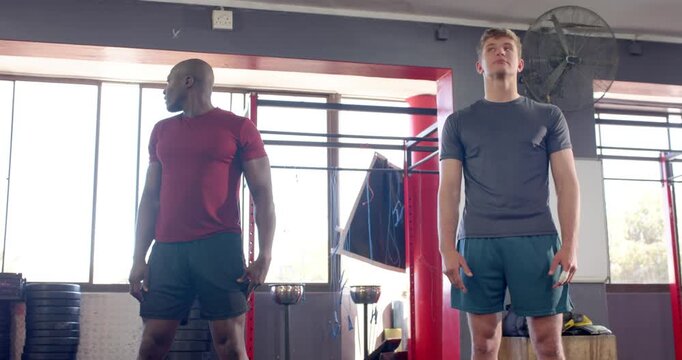 Male coach and trainee warming up, nodding heads, rolling shoulders, circling arms by squat rack