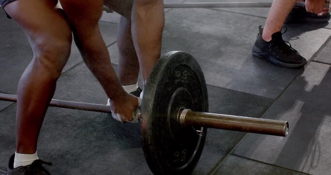 Diverse male partners dusting chalk, gripping, lifting barbell at gym for workout
