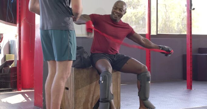 Diverse male duo receiving gloves and wraps, wrapping on box and preparing to spar in studio