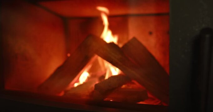 Flames dancing around logs catching fire inside metal stove firebox, releasing embers heating room