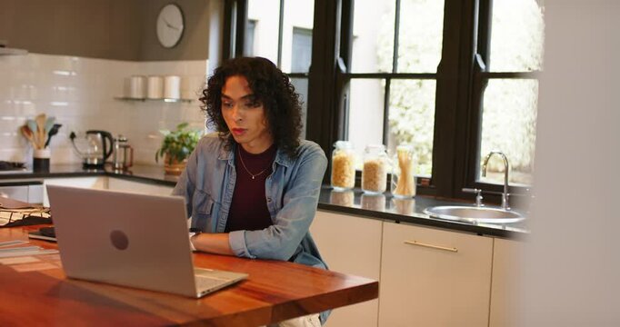 Opening laptop, non-binary person typing in kitchen, jotting in notebook with pen, capturing ideas