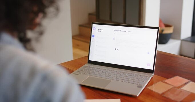 Non-binary person at desk scanning proposal template on laptop, tapping trackpad and sipping coffee