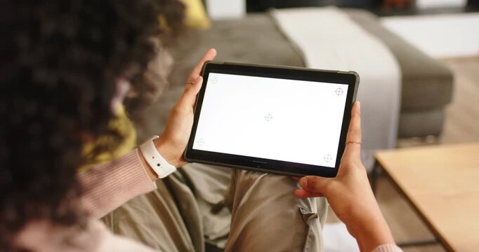 Adult non-binary person raising digital tablet on sofa, adjusting angle against overhead glare