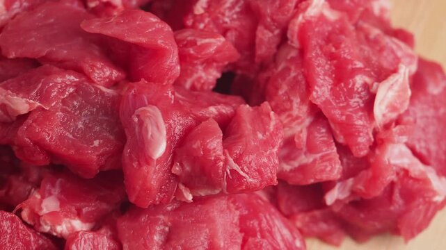 Raw chopped beef meat pieces piled on wooden cutting board for cooking