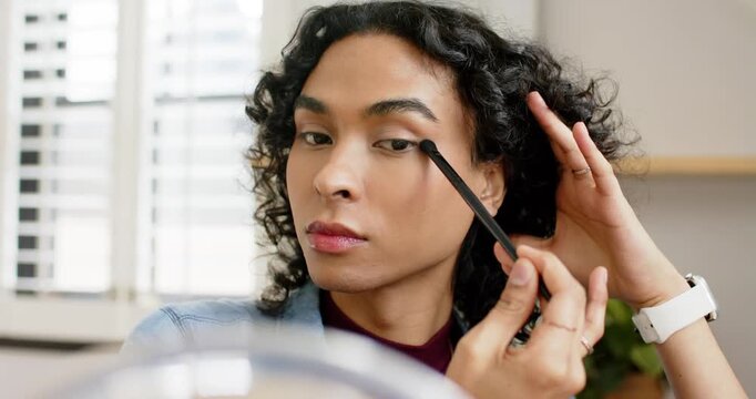 Holding brush with brown eyeshadow, nonbinary person blending crease for symmetry at vanity mirror