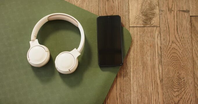 Upon camera start, headphones and smartphone are resting on exercise mat showcasing fitness gear
